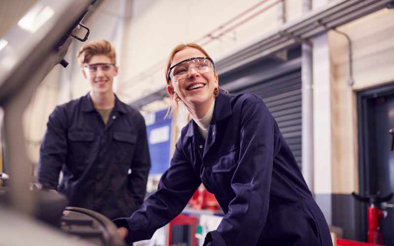 Male And Female Students Looking At Car Engine On Auto Mechanic Apprenticeship Course At College