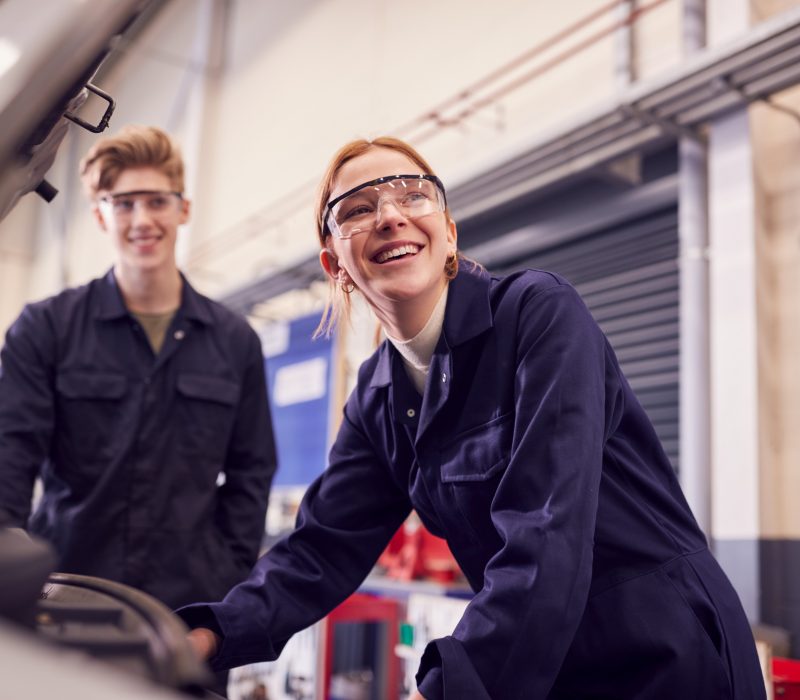 Male And Female Students Looking At Car Engine On Auto Mechanic Apprenticeship Course At College